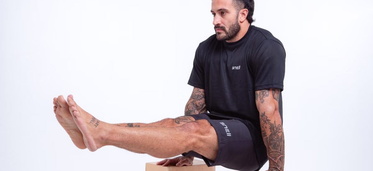 Man demonstrating strength in studio setting, wearing black sportswear and showcasing tattoos.