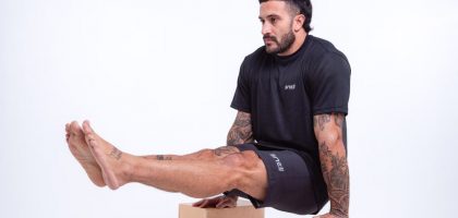Man demonstrating strength in studio setting, wearing black sportswear and showcasing tattoos.
