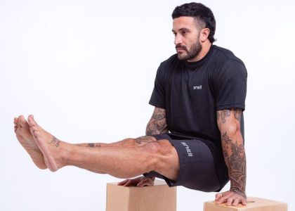 Man demonstrating strength in studio setting, wearing black sportswear and showcasing tattoos.
